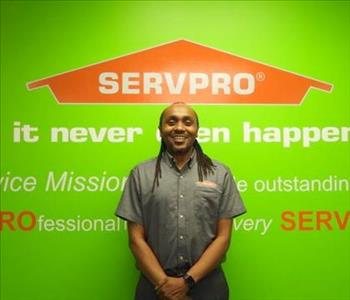 Male employee Eric Mwangi standing in front of a green wall with the SERVPRO logo and mission statement below it.