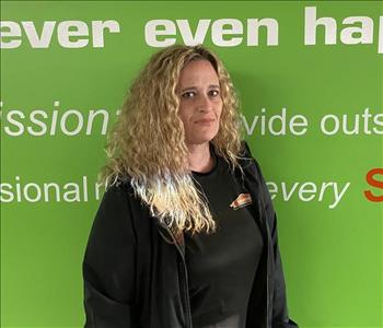 Female employee Trisha Burnette standing in front of a green wall with the SERVPRO logo