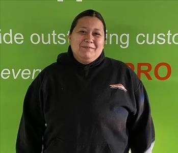 Female employee Imelda Barrera standing in front of a green wall with the SERVPRO logo